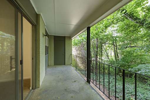 A balcony with a black railing and a view of a green forest.