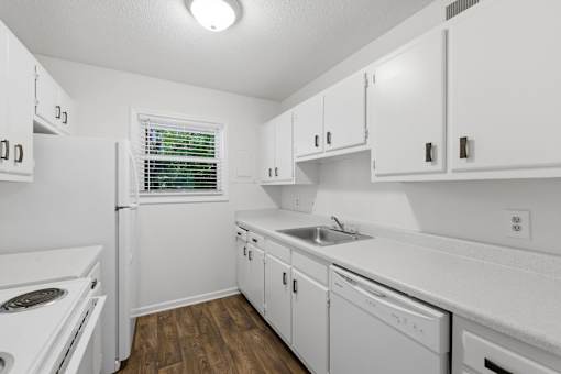 A white kitchen with wood floors and white appliances.