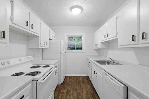 A white kitchen with wood floors and white appliances.
