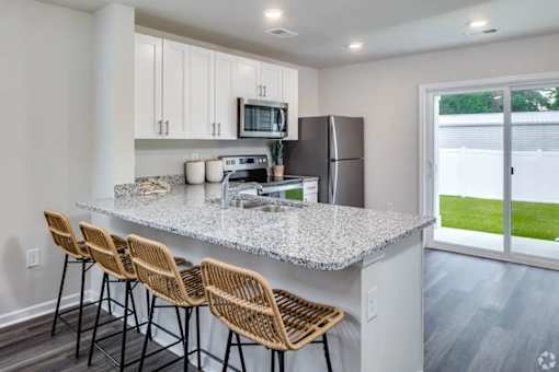 A kitchen with a granite countertop and wicker barstools.
