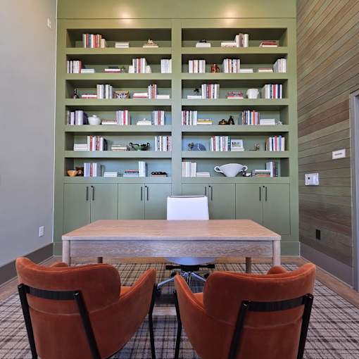 Two orange chairs are in front of a table and a bookshelf.