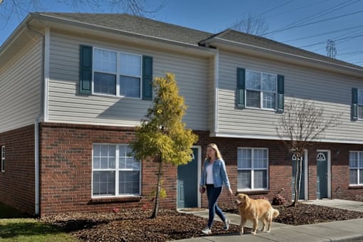 A woman walking her dog in front of a two-story house.