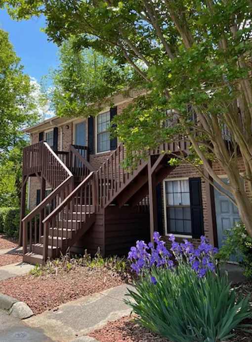 A house with a brown deck and a tree in front.