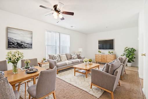 A living room with a grey couch, a wooden table, and a ceiling fan.