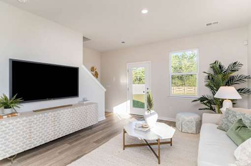 A living room with a white couch, a coffee table, and a flat screen TV mounted on the wall.