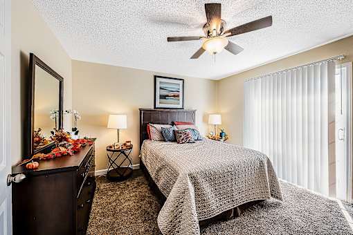 A bedroom with a bed, a dresser, a mirror, and a ceiling fan.