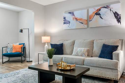 A living room with a grey couch, a blue chair, a black table, and two paintings on the wall.