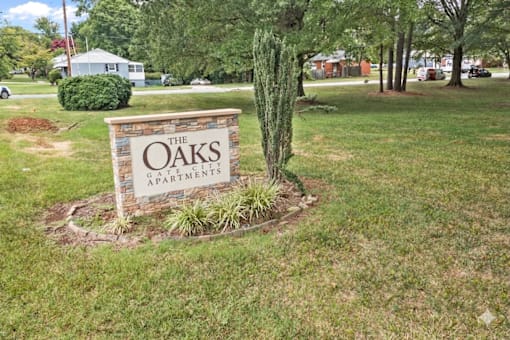 A sign for The Oaks Apartments is surrounded by a small garden.