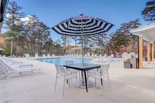 A poolside area with a table and chairs and a striped umbrella.
