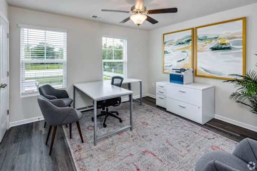 A room with a desk, chairs, and a ceiling fan.