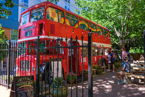A red double-decker bus is parked in front of a fence with a sign that says "Coffee Bus".