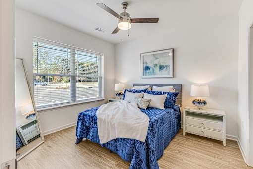 A bedroom with a blue bedspread and a ceiling fan.