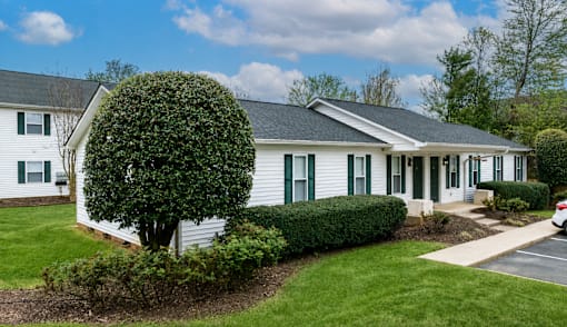 A white house with green shutters and a grey roof.
