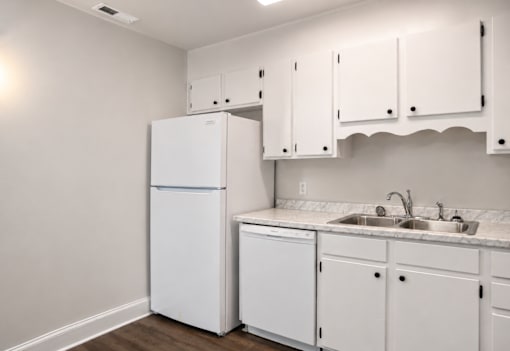 A white kitchen with a refrigerator, cabinets, and a sink.