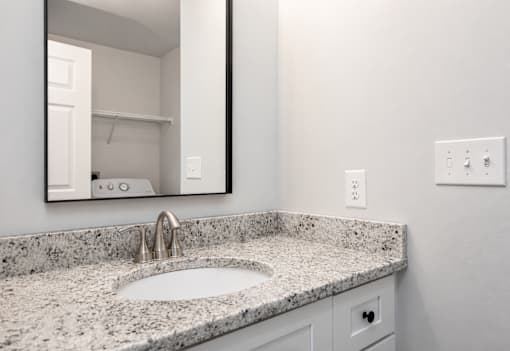 A bathroom sink with a granite countertop and a mirror above it.