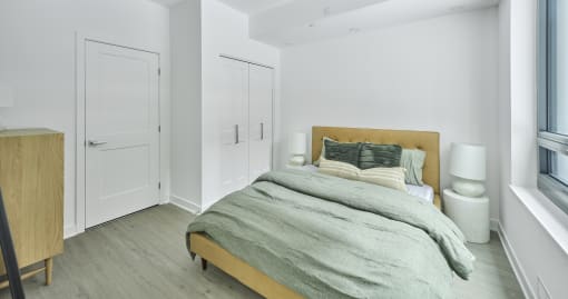 a bedroom with white walls and a bed with grey blankets and pillows