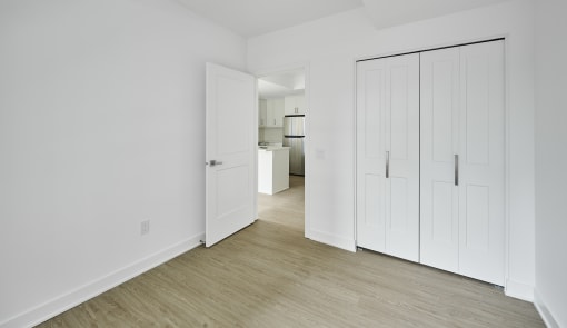 a bedroom with white walls and white closets and a wood floor