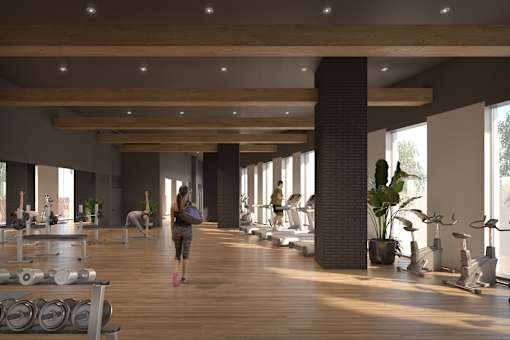 A woman is walking through a spacious gym with wooden floors and various exercise equipment.