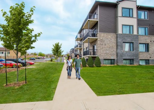 two people walking down a sidewalk in front of an apartment building