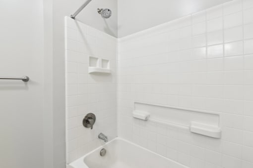 A white tiled bathroom with a shower head and a faucet.