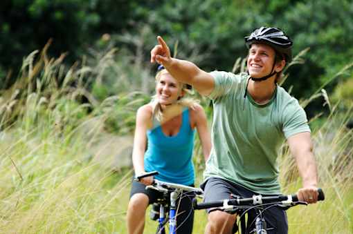 A man and a woman are riding bicycles in a grassy area.