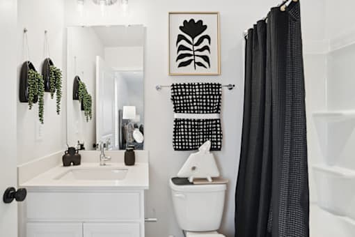 A white bathroom with a black and white towel hanging on the wall.