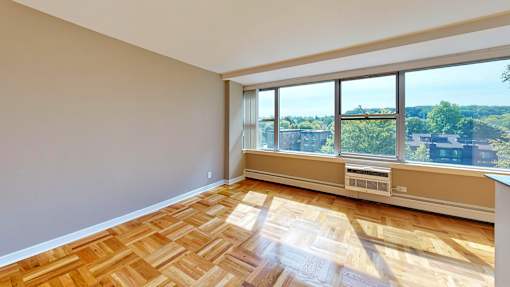A room with wooden flooring and a large window overlooking a cityscape.