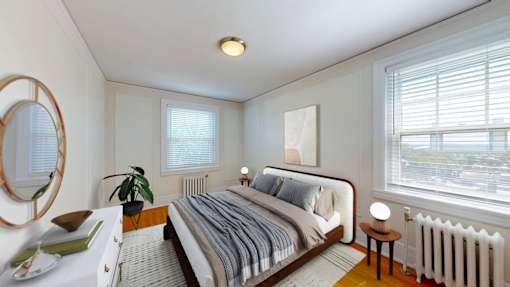 A bedroom with a bed, a mirror, a nightstand, and a window with blinds.