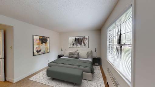 A bedroom with a bed, two pillows, a nightstand, and a window with blinds.