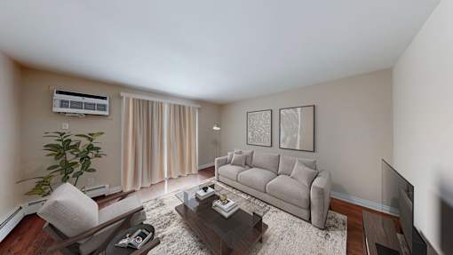 A living room with a grey couch, a coffee table, a plant, and a television.