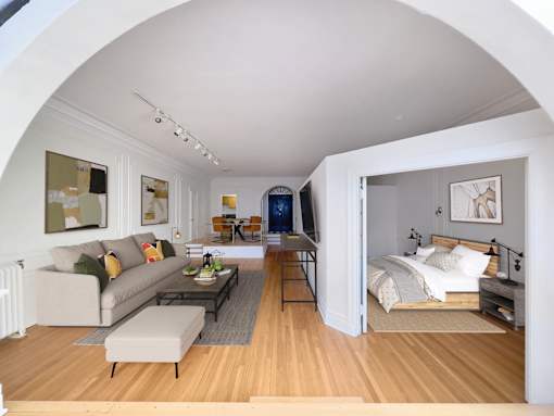A living room with a couch, a coffee table, and a bed in the background.