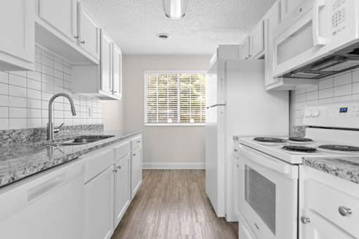 A kitchen with white cabinets and a marble countertop.
