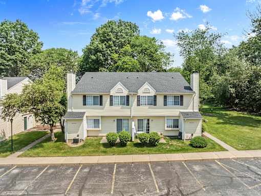 A two-story house with a large front yard and a parking lot in front.