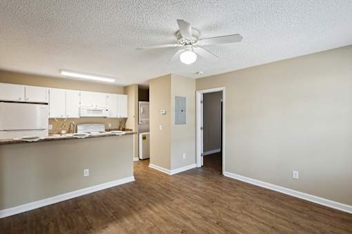 A room with a ceiling fan and a kitchen area with cabinets and a counter.