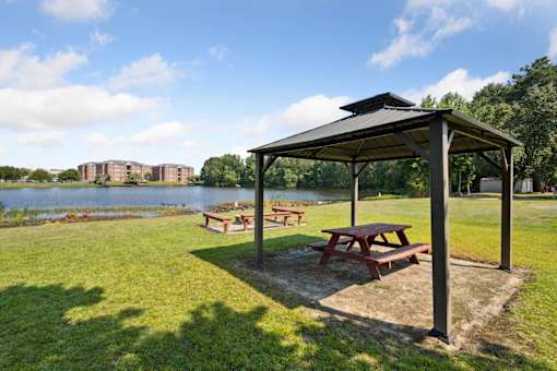 Picnic table and pavillion in a park with a lake in the background.