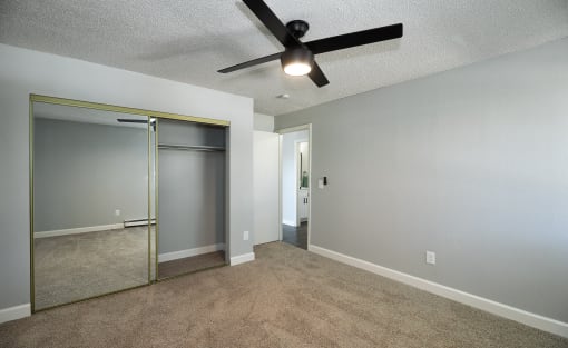 an empty living room with a ceiling fan and a mirrored closet