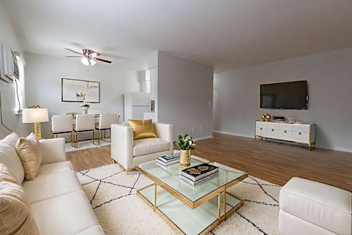 A living room with a white couch, a glass coffee table, and a television on the wall.