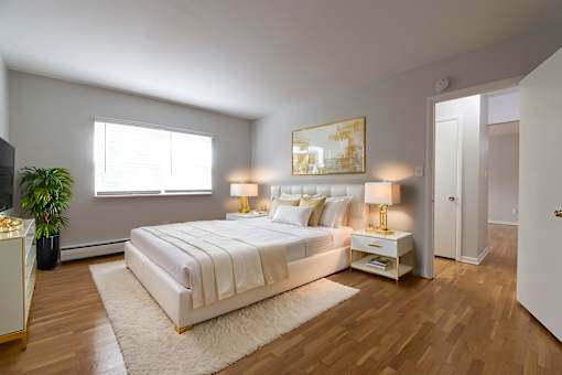 A bedroom with a large bed, a potted plant, and a painting on the wall.