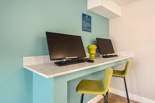 Two laptops are on a desk with a green chair.