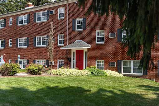 A red brick building with a red door and green bushes in front.