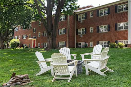Four white chairs are placed on a lawn in front of a red brick building.