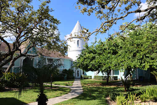 A white building with a tower is surrounded by green trees.