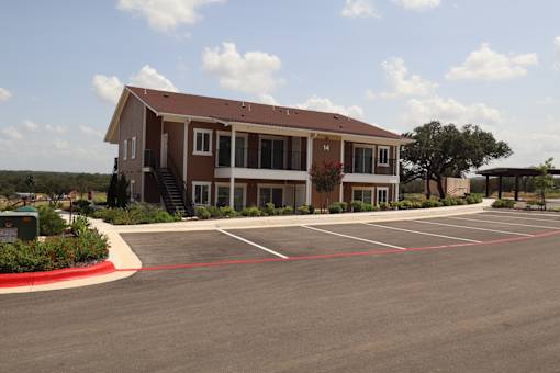 A brown building with a red roof and a parking lot in front.