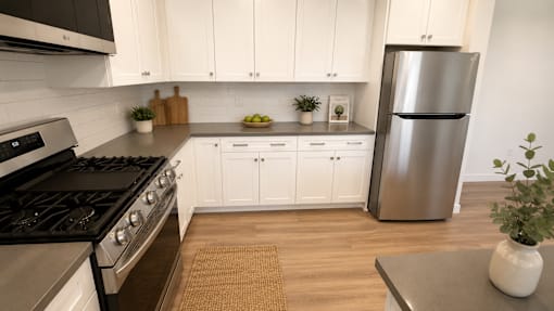 A modern kitchen with a stainless steel refrigerator, wooden floors, and white cabinets.