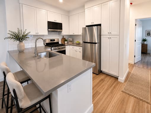 A kitchen with a stainless steel refrigerator and a countertop with a sink and two chairs.