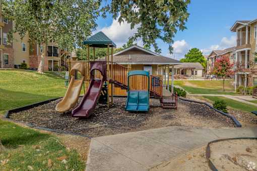 A playground with a slide, swings and a playhouse at The Villages at Lost Creek Apartments, San Antonio, Texas