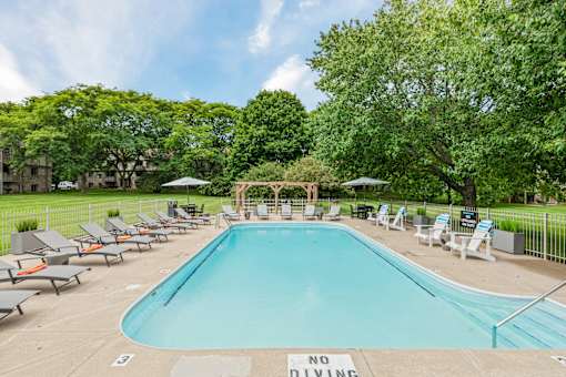 A pool surrounded by lawn chairs and trees with a sign that says no diving.