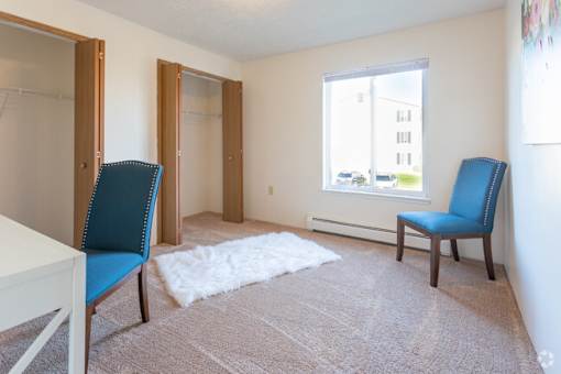 A room with a white table, two blue chairs, and a white rug.