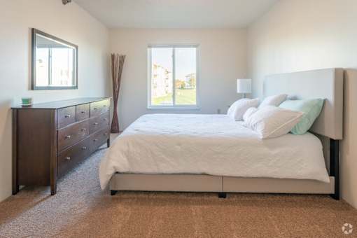 A bedroom with a bed, dresser, and window.