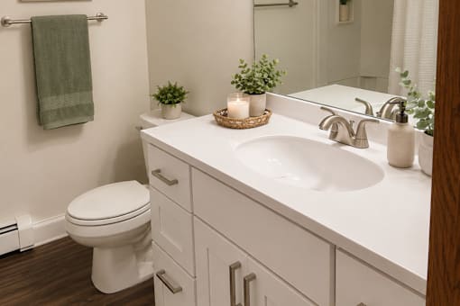 A white bathroom with a toilet, sink, and a green towel hanging on the towel rack.